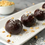 Salted chocolate protein balls topped with shredded coconut and peanuts on a white plate
