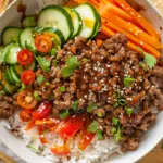 Hot honey ground beef bowls with glazed caramelized beef over white rice, fresh cucumber slices, cherry tomatoes, and julienned carrots in white bowl