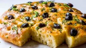 Olive and herb focaccia bread topped with olives, fresh herbs, and olive oil, baked until golden and fluffy