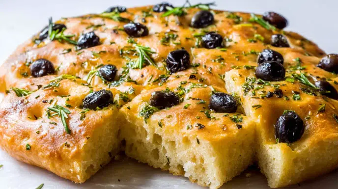 Olive and herb focaccia bread topped with olives, fresh herbs, and olive oil, baked until golden and fluffy
