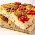 Homemade tomato basil focaccia bread topped with fresh cherry tomatoes, basil leaves, and olive oil