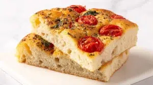 Homemade tomato basil focaccia bread topped with fresh cherry tomatoes, basil leaves, and olive oil